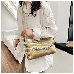 Detail of golden pleated bag with metallic finish and silver chain strap on a model