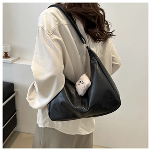 Detail of black leather crescent underarm bag with a cute white plush bear pendant