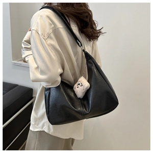 Detail of a black matte leather hobo tote bag featuring a cute white plush puppy charm