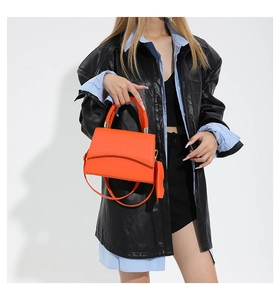 Detail view of vibrant orange crocodile texture handbag with woven handle and side charm