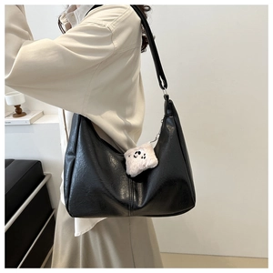 Close-up of black glossy leather hobo bag with a cute plush panda charm on shoulder strap