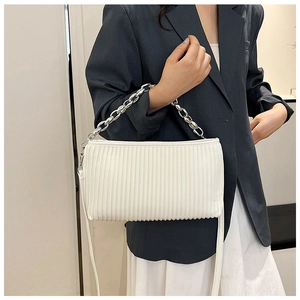Close-up of pleated white baguette bag with silver chain strap on model in grey suit
