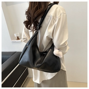 Close-up of black leather tote bag with lychee texture and plush white charm accessory