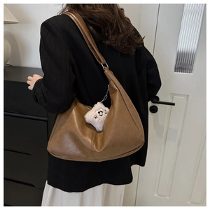 Detail of brown matte leather shoulder bag featuring a cute white plush bear pendant