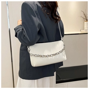 Detailed view of white pleated shoulder bag with silver chain worn over a dark blue suit