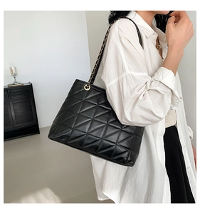 Detail of black quilted PU leather tote bag with elegant gold chain strap worn by a model
