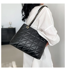 Detail of black quilted tote bag with gold chain strap shown on a model