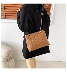 Close-up of brown quilted leather tote bag with gold chain strap on a black blazer