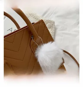 Detail of a brown leather handbag with V-quilting and a soft white faux fur pompom charm