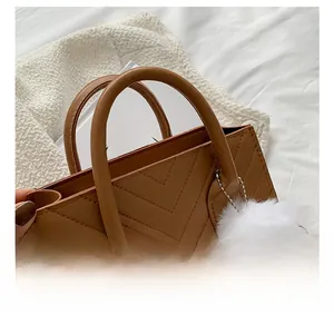 Close-up of brown quilted leather bag featuring gold rings and soft white pom-pom detail