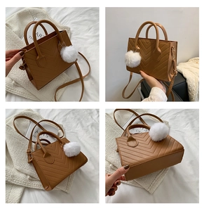 Brown quilted crossbody bag with chevron stitching, plush ball charm and top handles