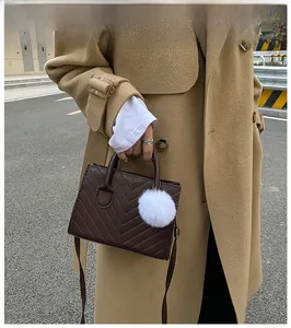 Vista da strada di una borsa trapuntata marrone scuro con pompon in ecopelliccia bianca