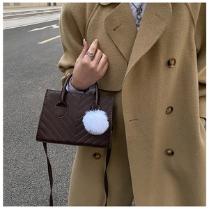 Dettaglio borsa trapezoidale marrone scuro con trapuntatura a V e pompon bianco