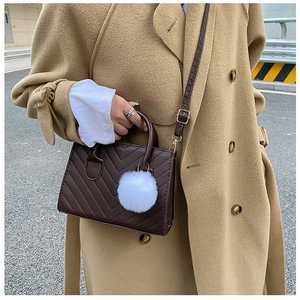 Detail of dark brown quilted crossbody bag with white faux fur pompom charm on a model