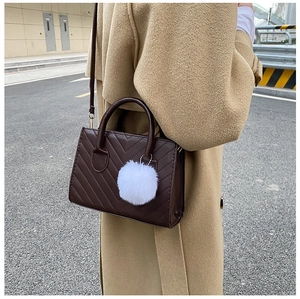 Dettaglio borsa trapuntata a V marrone scuro con pompon bianco su outfit con trench coat