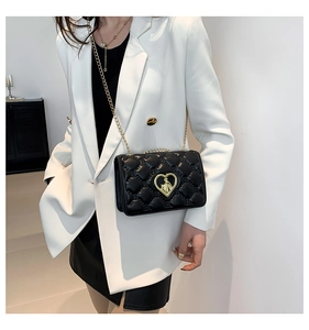 Detail view of black quilted chain crossbody bag with a gold heart-shaped metal clasp