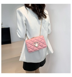 Detail of pink quilted crossbody bag with heart-shaped metal lock on white blazer