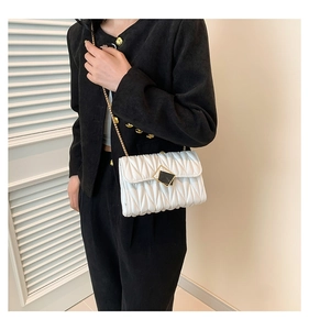 Détail d'un sac à bandoulière matelassé blanc avec chaîne dorée et boucle métallique carrée