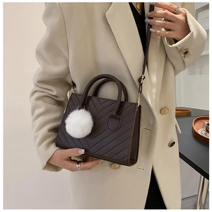 Dettaglio di una borsa a tracolla marrone scuro con trapuntatura a V e pompon in peluche