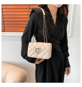 Detail of quilted beige crossbody bag featuring a golden heart-shaped twist lock buckle