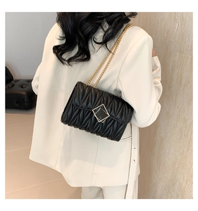 Mannequin portant un sac à bandoulière matelassé noir avec boucle dorée sur un blazer blanc