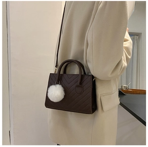 Dettaglio della borsa squadrata trapuntata marrone scuro con ciondolo in peluche e cappotto
