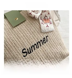 Detail of beige woven bag featuring Summer embroidery, leather flap and silk scarf