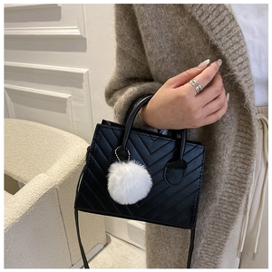 Dettaglio borsa a mano nera trapuntata a V con ciondolo a pompon bianco e tracolla