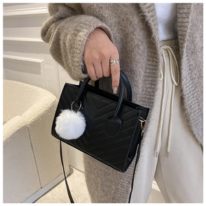 Detail of black V-quilted handbag with white faux fur pompom and adjustable strap