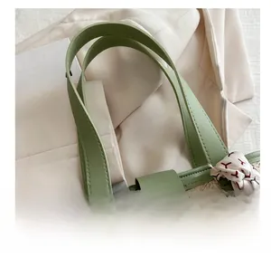 Detail of woven straw tote bag with avocado green leather handles and silk scarf accent