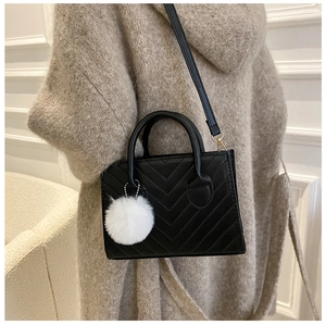 Detail of black V-quilted handbag with white pom-pom charm and removable shoulder strap