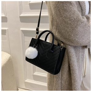 Detail of black V-quilted faux leather crossbody bag with fluffy white pompom charm
