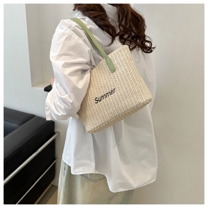 Detail of woven straw tote bag with green handles and Summer embroidery on white background