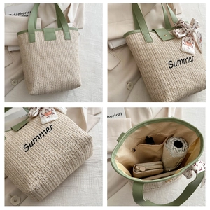 Detail view of woven straw tote bag with green handles and embroidered Summer text