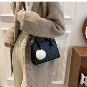 Dettaglio della borsa a tracolla nera trapuntata con pompon bianco su un outfit casual
