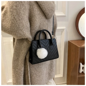 Dettaglio borsa nera con cuciture a V e ciondolo a pompon bianco decorativo