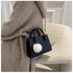Dettaglio borsa a tracolla nera con trapuntatura a V e ciondolo pompon bianco in peluche