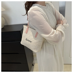 Detail of woven straw tote bag featuring pink handles and black Summer embroidery