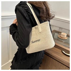 Detail of a woven straw tote bag with Summer embroidery and slim shoulder straps