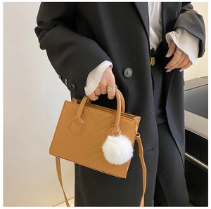 Dettaglio della borsa quadrata color cuoio con trapuntatura a V e ciondolo di peluche