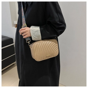 Detail of beige quilted crossbody bag featuring a colorful geometric wide shoulder strap