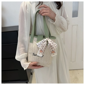 Close-up of woven straw handbag with Summer embroidery and green handles with silk scarf