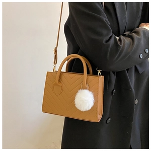 Detail of tan chevron quilted crossbody bag with top handles and plush white pompom