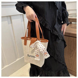 Detail of woven straw tote bag featuring Summer embroidery and silk scarf handle