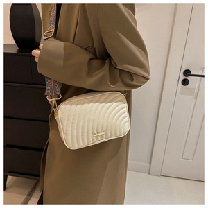 Detail of quilted crossbody bag with wide ethnic pattern strap and golden hardware