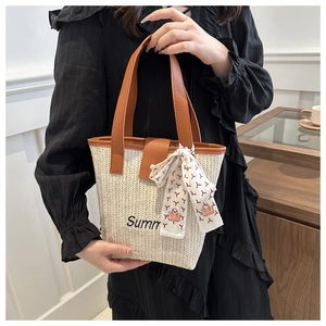 Close-up of woven straw tote bag featuring leather handles and decorative silk scarf