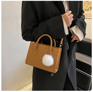 Dettaglio borsa in pelle marrone con cuciture a V e ciondolo a pompon bianco soffice