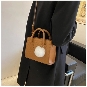 Detail of caramel brown quilted square bag with plush charm and detachable strap