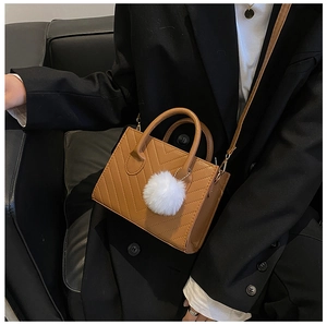 Detail of caramel crossbody bag with herringbone quilting and white plush charm on a model