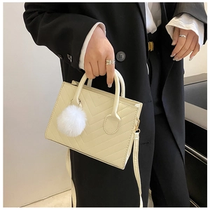 Dettaglio borsa a tracolla trapuntata beige crema con pompon bianco e finiture dorate